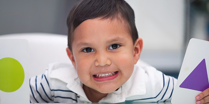 toddler boy holding cards with colored shapes, looking directly at the camera, smiling; credit: Shutterstock