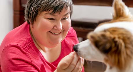 stock photo; adult woman with IDD, smiling, feeding a dog a treat; credit: Adobe Stock.
