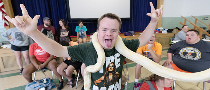 Young man with hands in the air, excited to be holding a snake around his neck during a wildlife encounter.