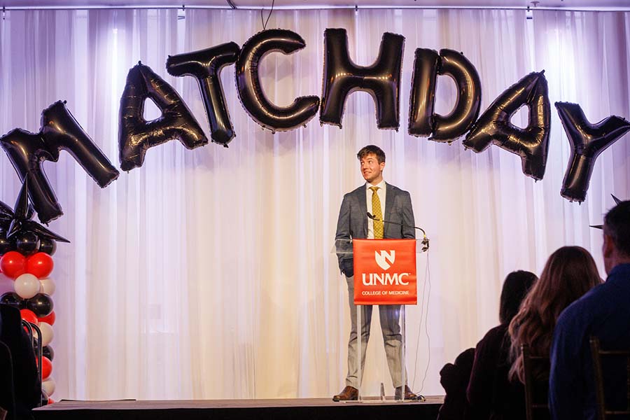 A medical student announces his residency match below a balloon sign spelling out "Match Day"