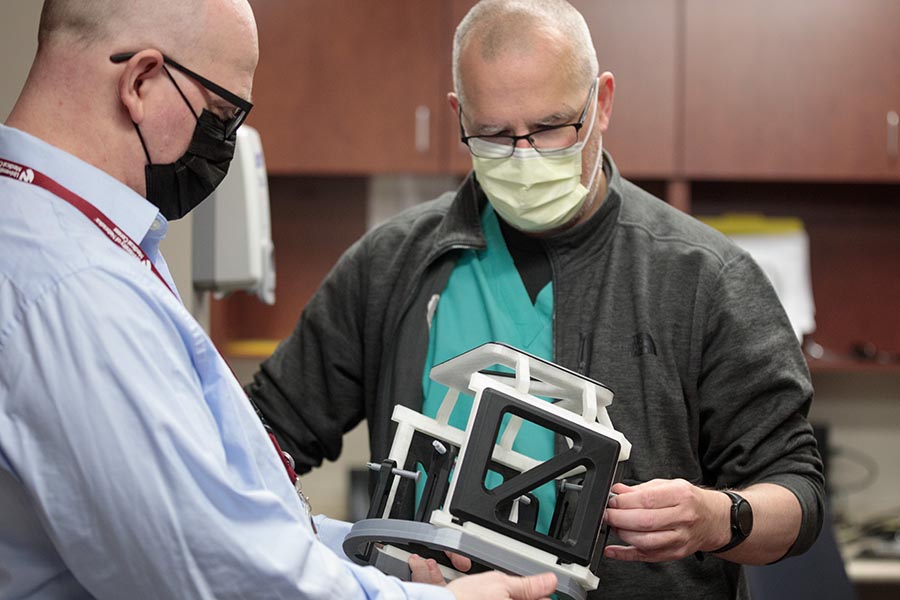 The replica head frame, held by Brian Maass, left, of the McGoogan Health Sciences Library’s makerspace, is making a difference, said Dennis Rieke of the UNMC Department of Neurosurgery.
