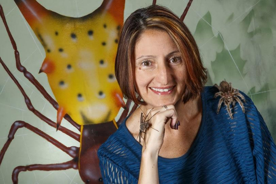 Eileen Hebets, PhD, in front of an illustration of a spider.