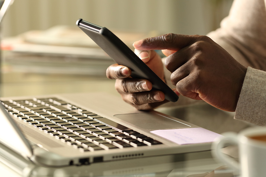 Person dialing a mobile phone in front of laptop