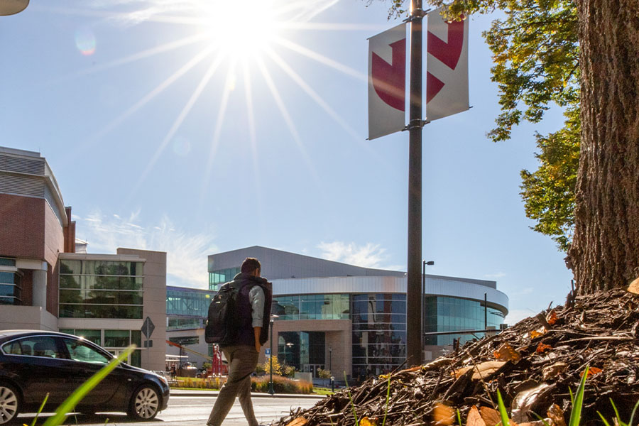 Student walking on sidewalk with sun shining