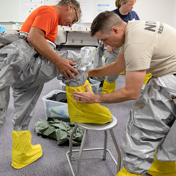 Two trainees put on biohazard equipment