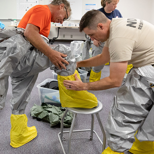 Two trainees put on biohazard equipment