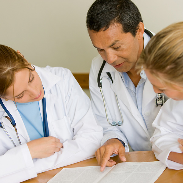 Doctor and two students sit at table looking at a folder