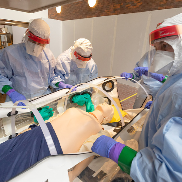 Trainees in full biohazard gear stand around a manikin in a mobile biocontainment unit