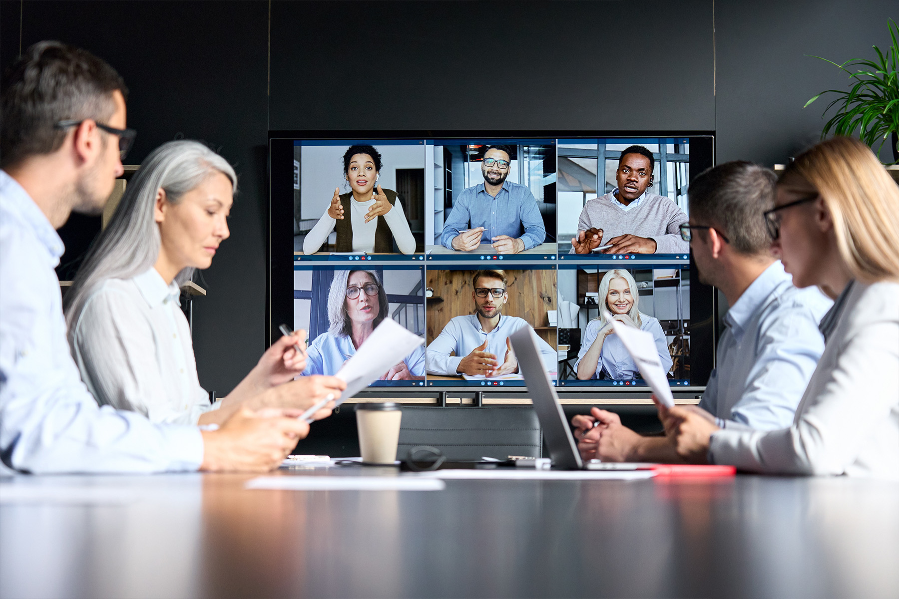 People talk around conference room looking at online attendees on tv screen