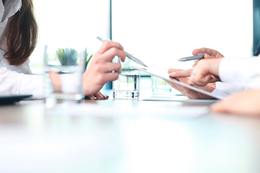 Two people sit at a table while one points at information on a clipboard