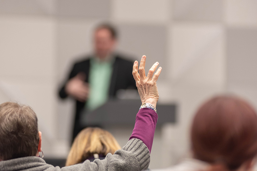 A person raises their hand during a conference to ask the speaker a question.