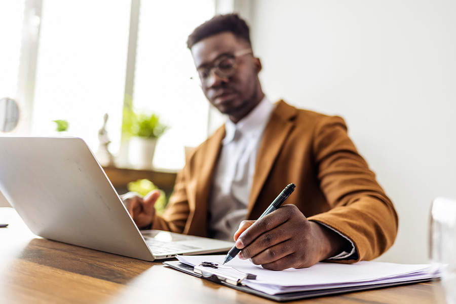 Man sits at computer and writes in notebook on desk