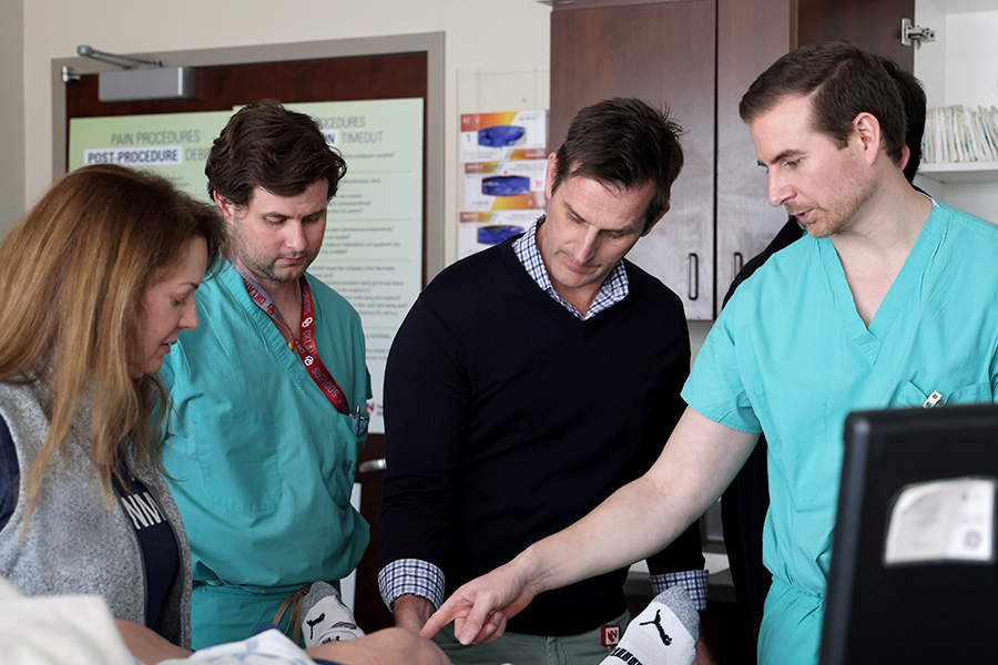 Faculty train two fellows on an ultrasound-guided procedure in a clinical setting.
