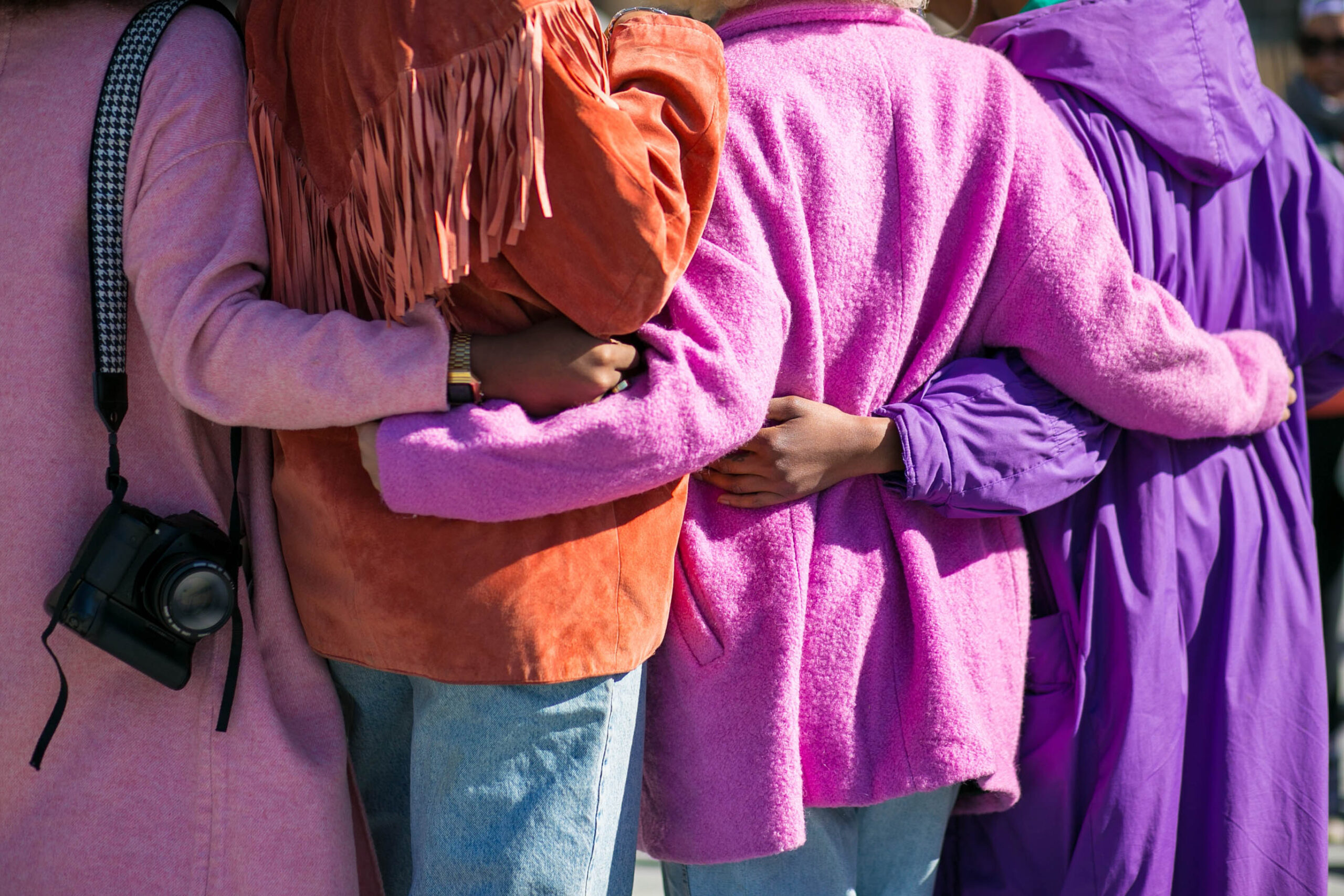 A view of four women in pink and purple coats hugging supportively.