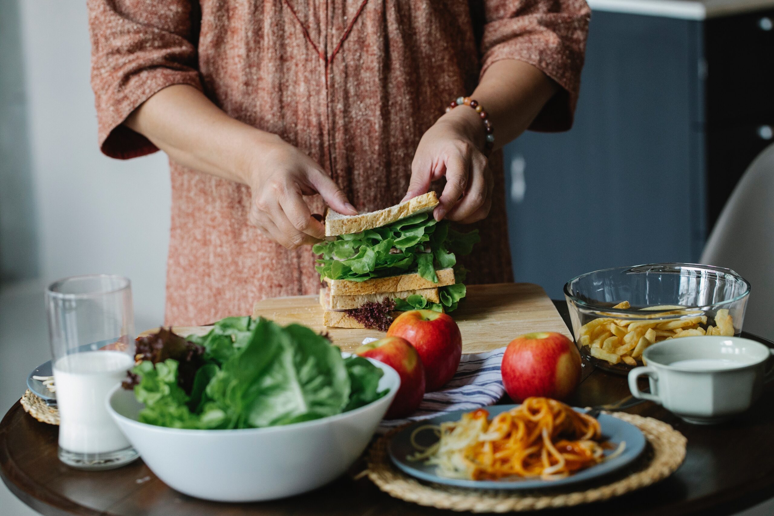 woman preparing a sandwich on a table of healthy foods