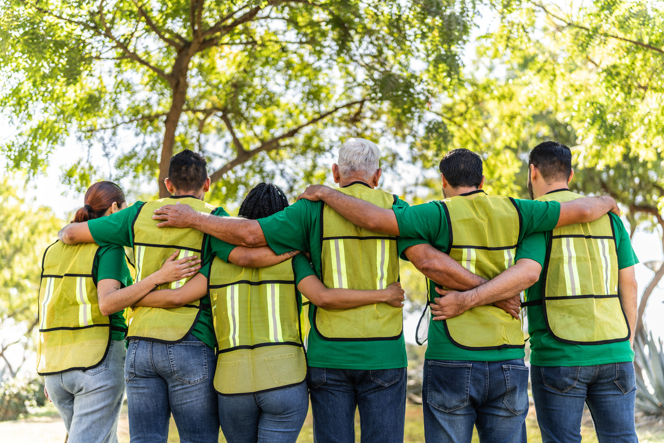 Group of volunteers in safety vests standing together with arms around each other, representing community support and recovery after a natural disaster.