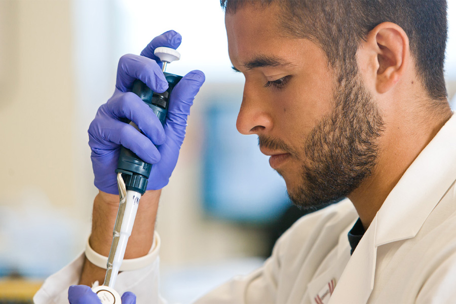 A student wearing rubber gloves holds a pipette