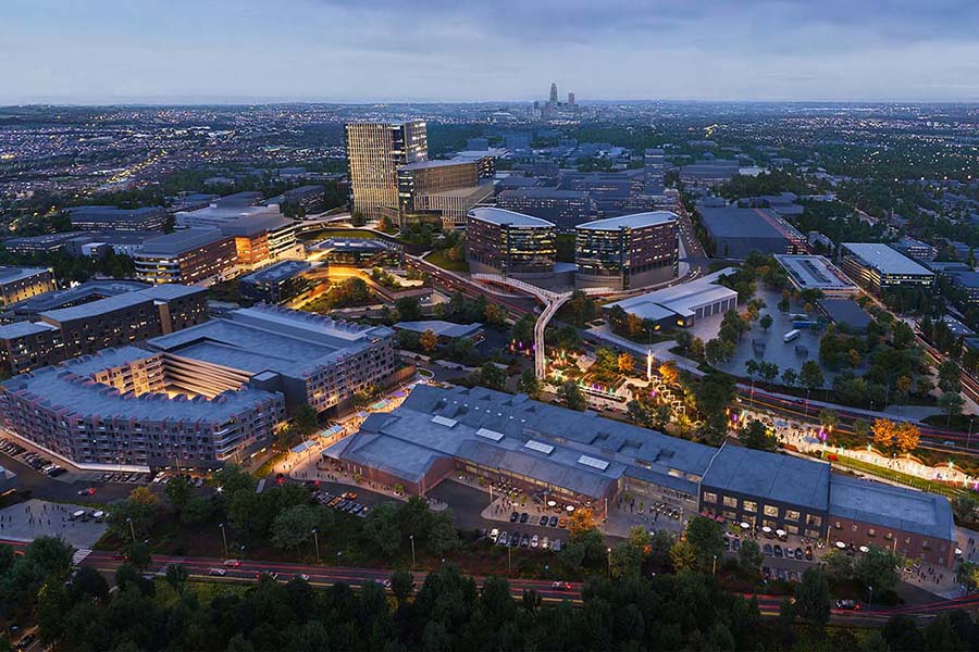Aerial view of campus at night showing the EDGE District with the new Catalyst and CORE buildings in the foreground and the Fred & Pamela Buffett Cancer Center and the Durham Research towers in the middle ground across the remainder of campus, with a view of the Omaha downtown skyline beyond.
