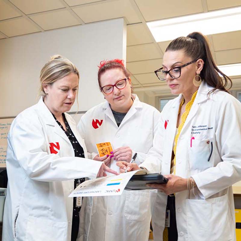 Three female faculty members reviewing safety information in a lab.