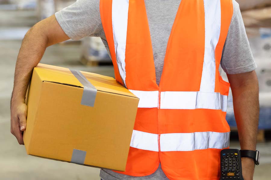 Worker in an orange safety vest holding a box under his right arm.