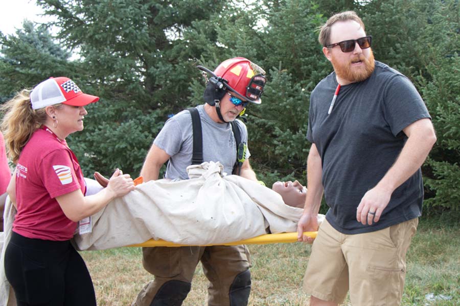 Three trainees carry a simulated patient on a stretcher during a disaster exercise.