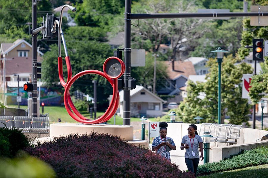 Two UNMC employees walk past a statue of a stethoscope on the UNMC campus