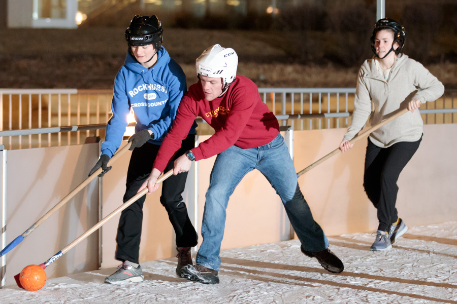 Three students play broomball on an ice rink