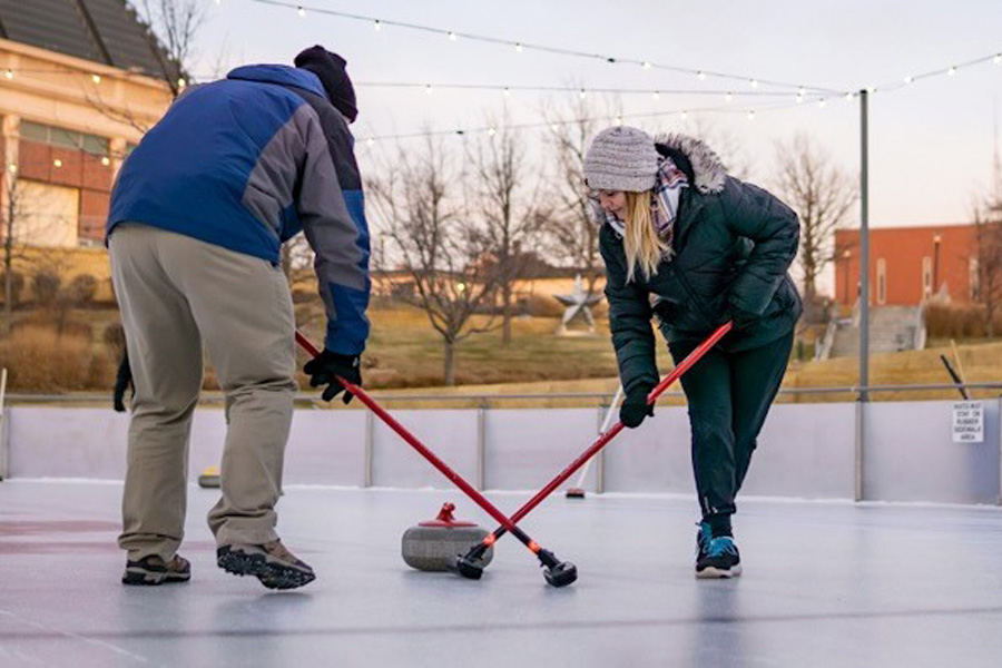 Two people participate in curling on an ice rink
