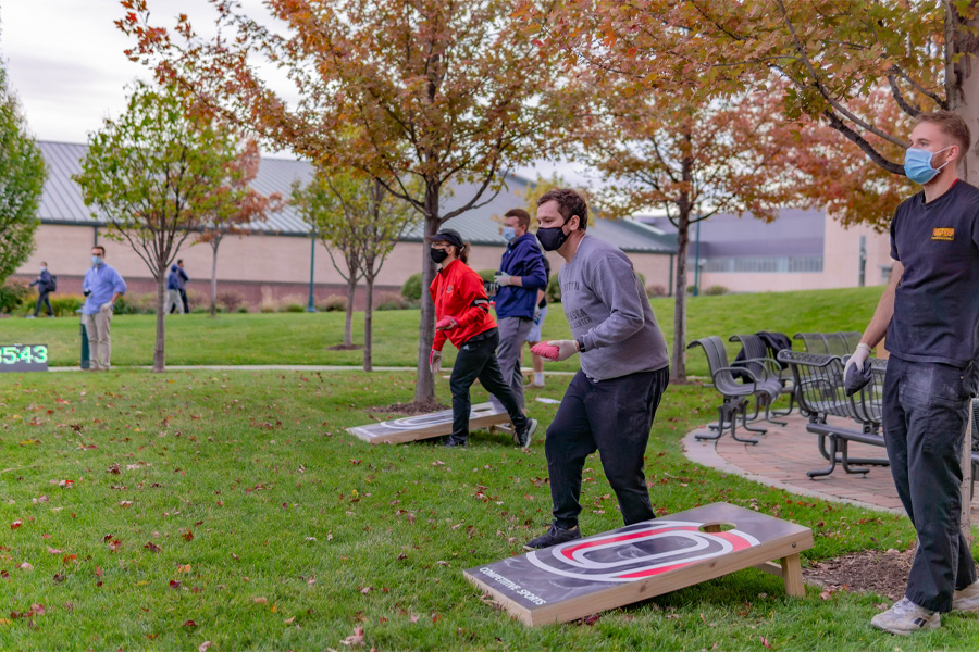 Four people throw bean bags while playing cornhole outdoors