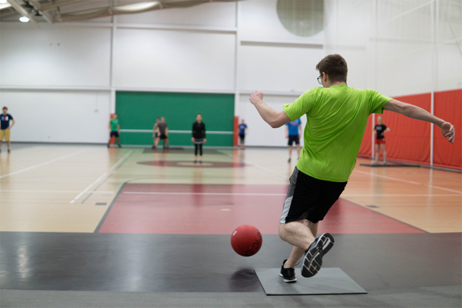 A man kicks a rubber ball while players in a gymnasium look on