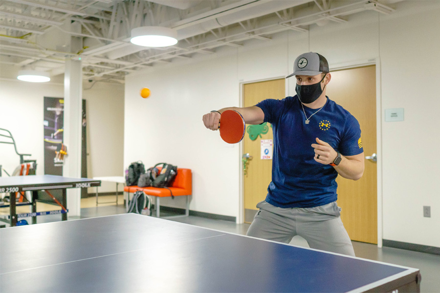 A man wearing a cloth mask prepares to hit a ping pong ball