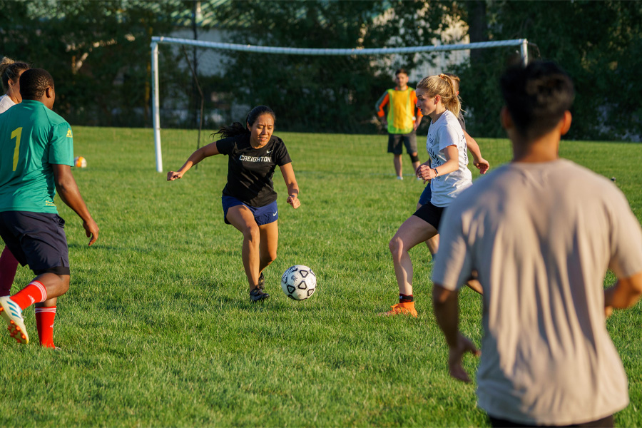 A group of people play soccer with a dark-haired woman in the act of kicking the ball