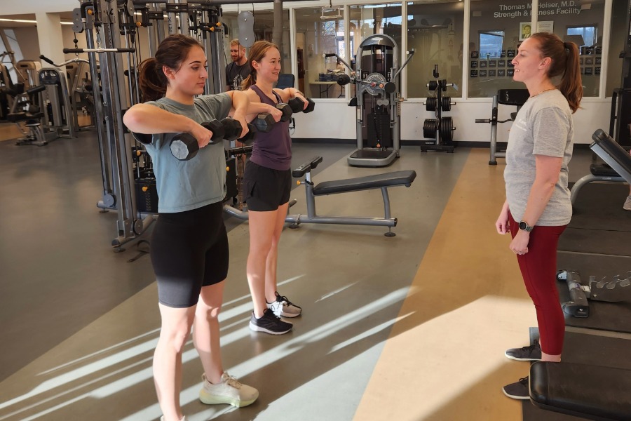 two female students lift weights with a personal trainer
