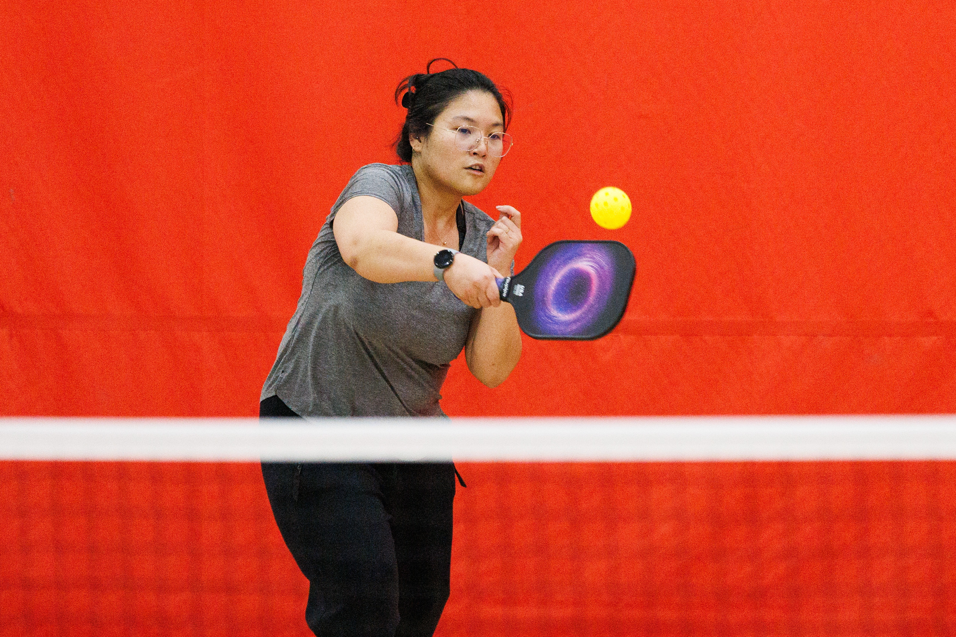 A female student hits a pickleball across the net