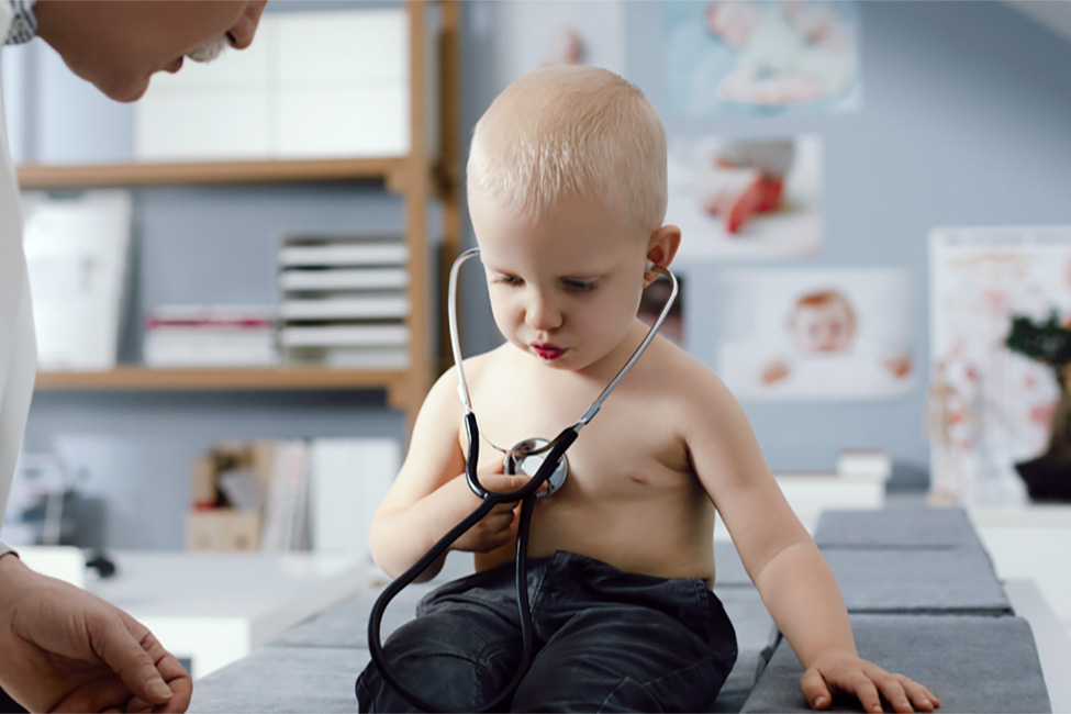 boy sitting on examination table as doctor listens to his heart