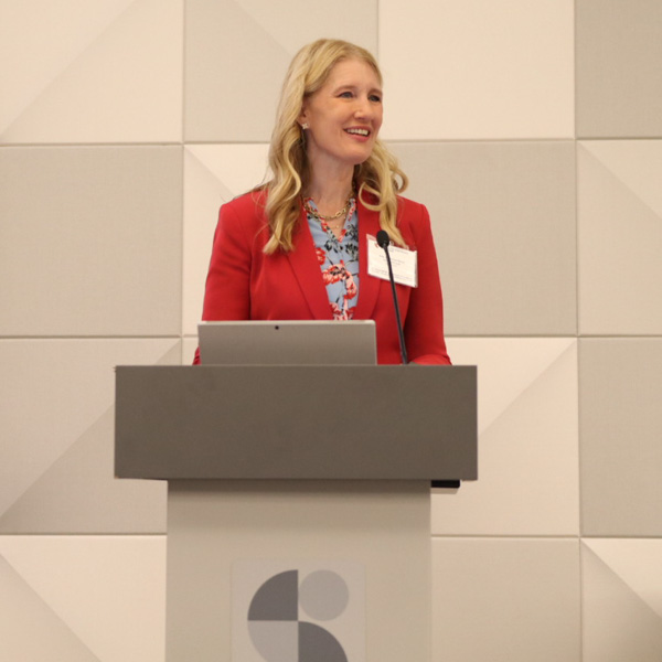 a woman at a podium talking to crowd with slides behind her