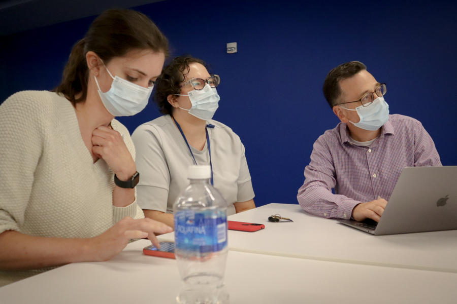 three people sitting at a table work on a writing project 