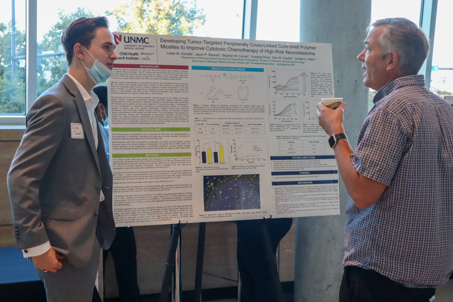 man asks questions to another man standing in front of a scientific poster