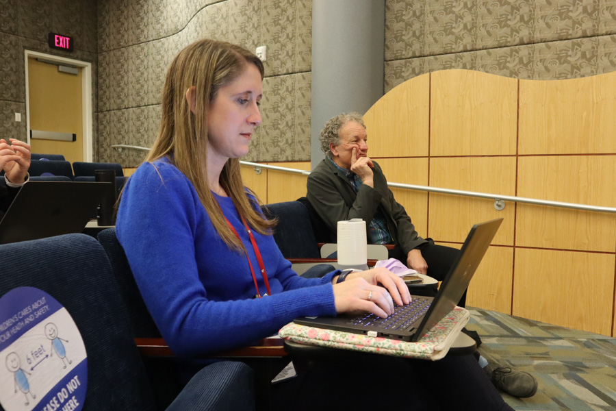 young woman sitting in an auditorium typing on the computer