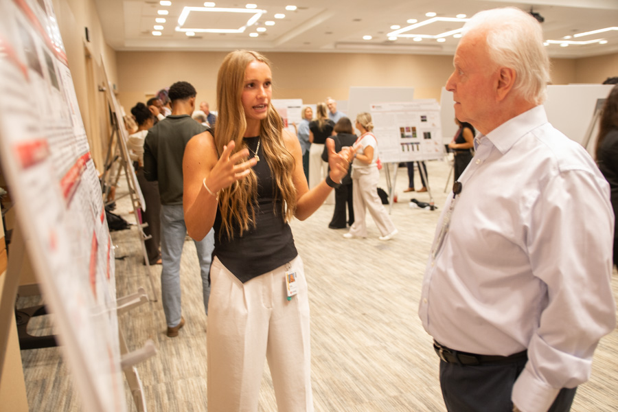 young woman talks to older man in front of research poster
