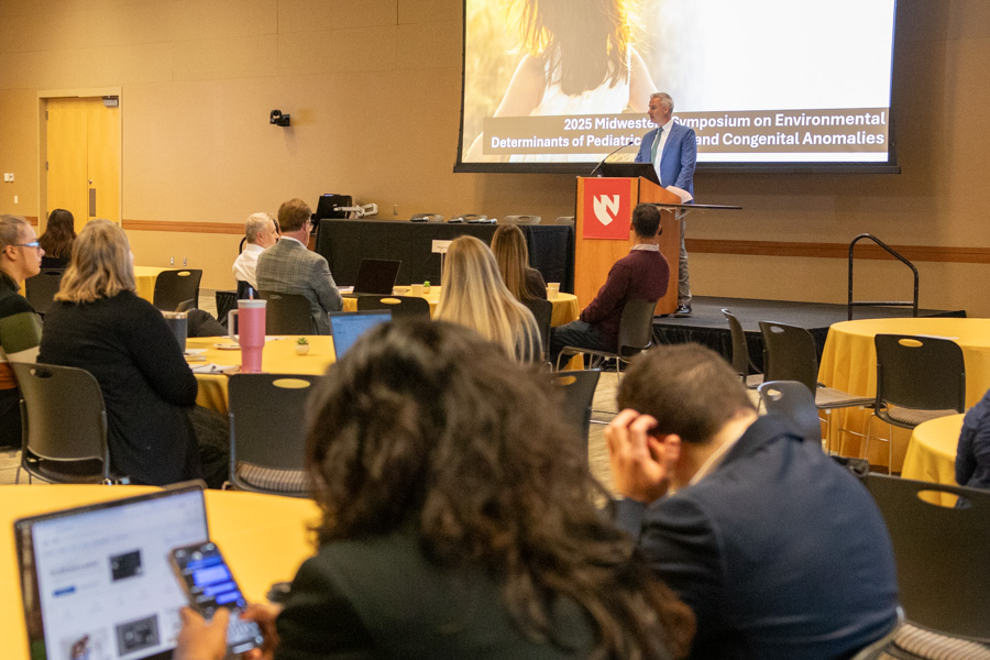 man stands at podium and address people at sitting at round tables
