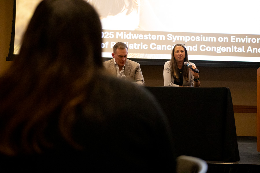 a man and a woman speak as part of a panel on stage