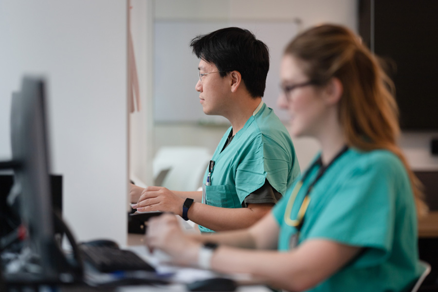 Two students in scrubs work on computers