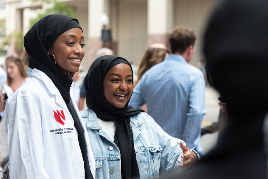 Two students wearing head scarves and white medical coats pose for a photo