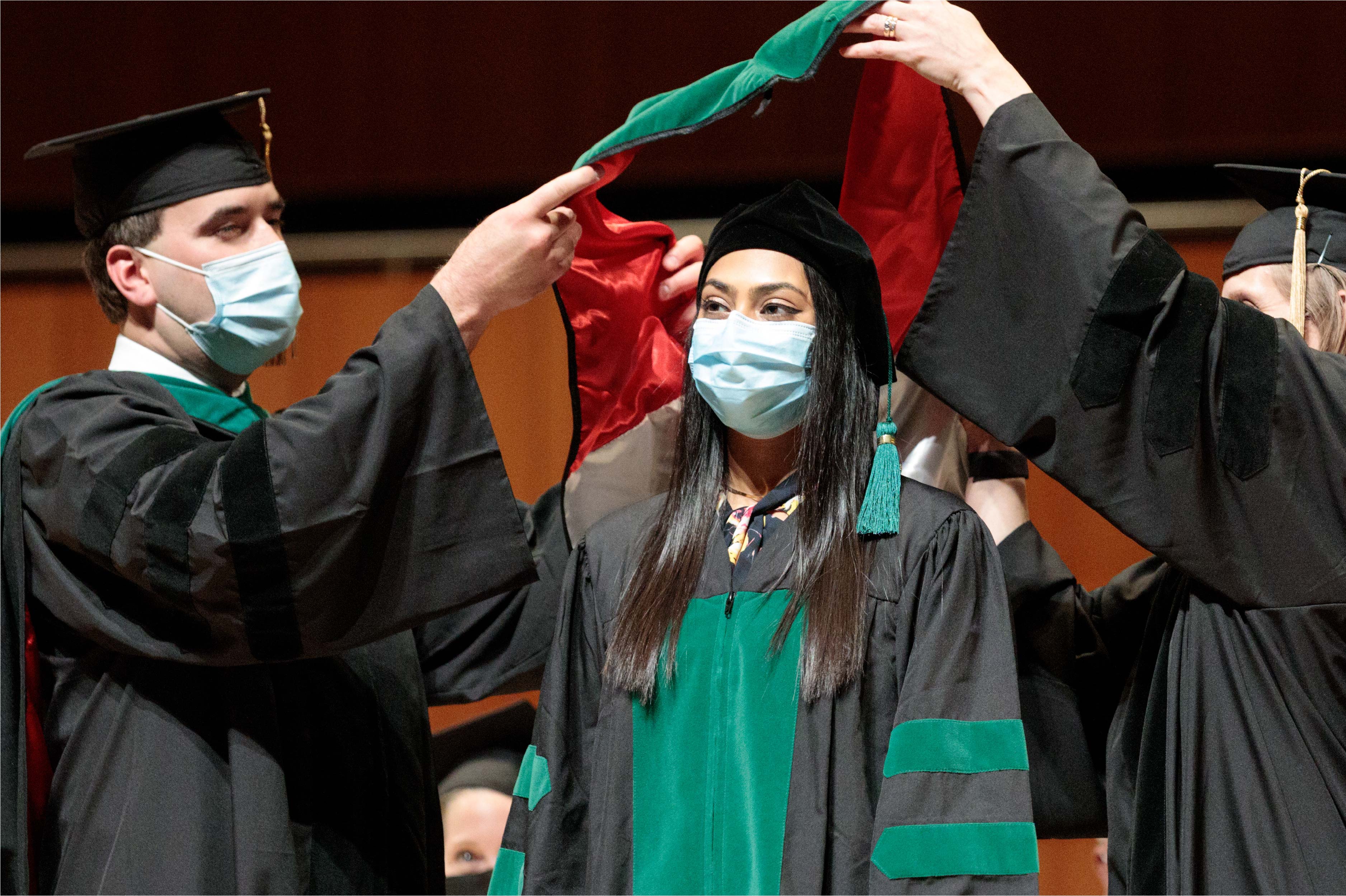 A student wearing graduation robes participates in a hooding ceremony
