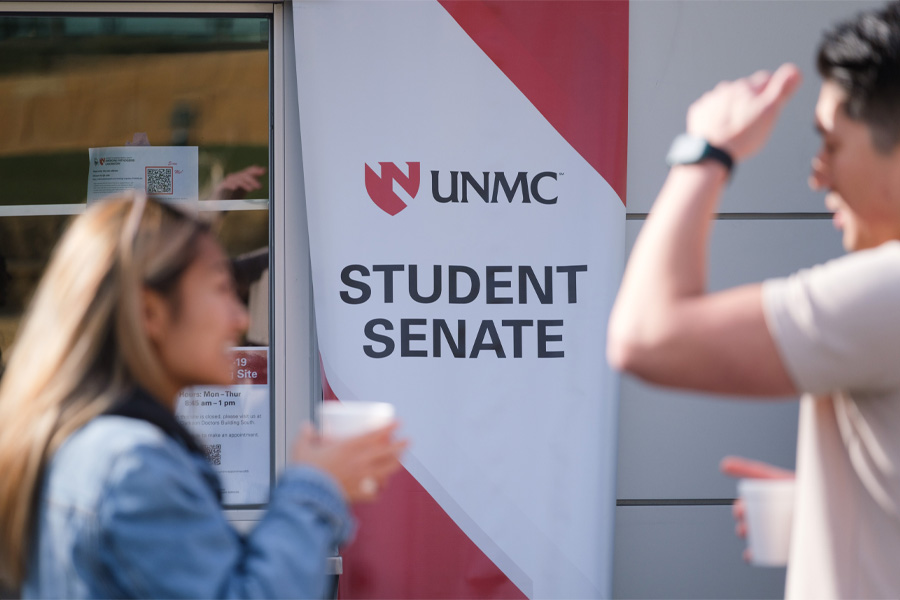 Two students speak in front of a banner that reads "UNMC Student Senate"