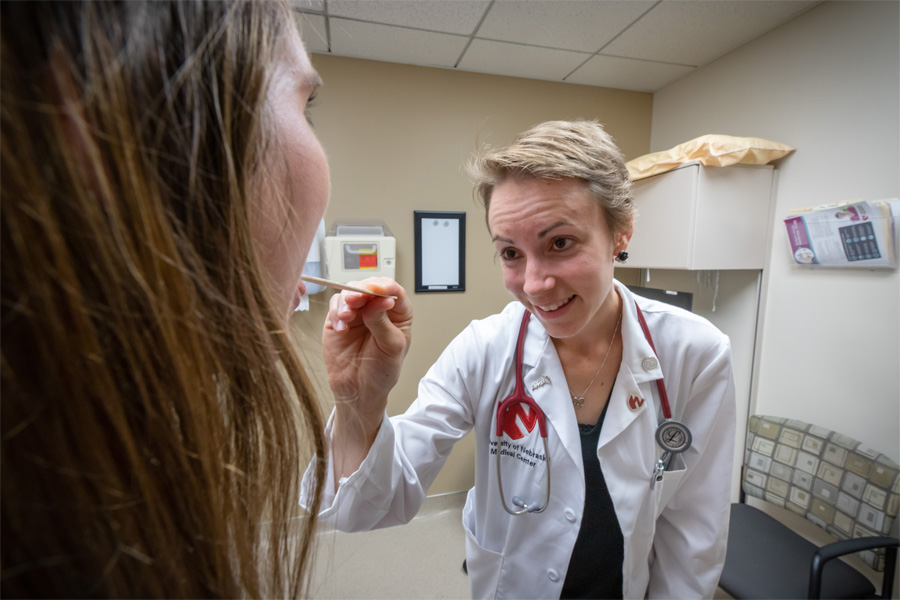 A woman wearing a doctor's coat looks at a patient's throat