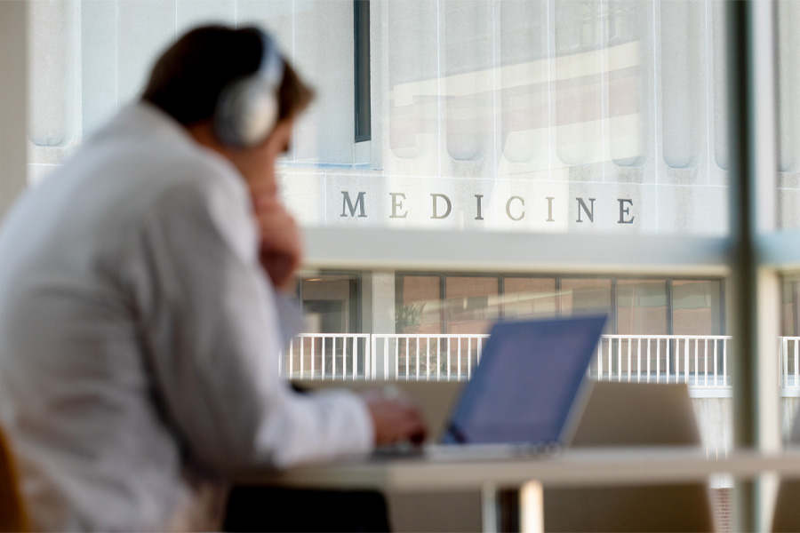 A student studies on a laptop, with the word "medicine" visible on a building in the background