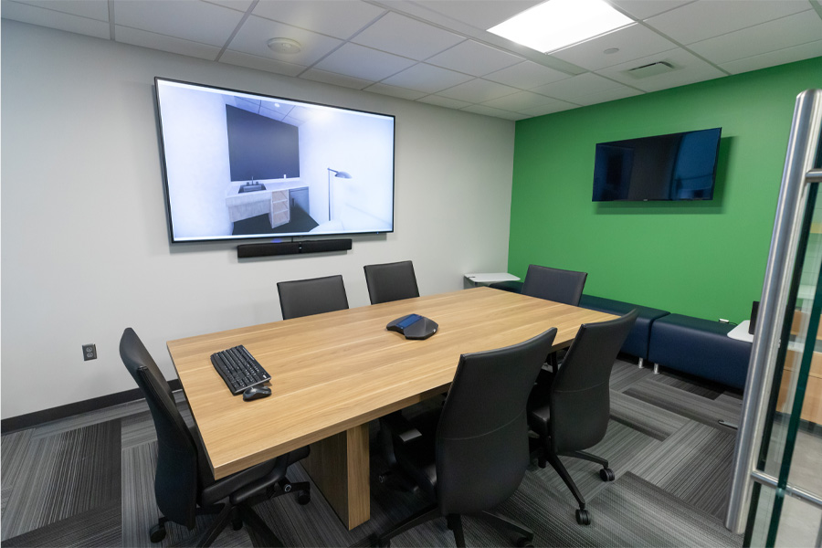 A conference room with six chairs surrounding a table and two display screens