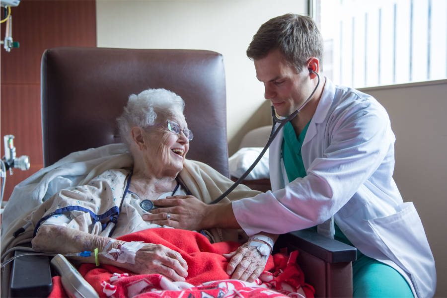 A male physician uses a stethoscope on an elderly female patient